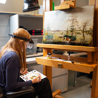 Conservator sitting at easel with painting